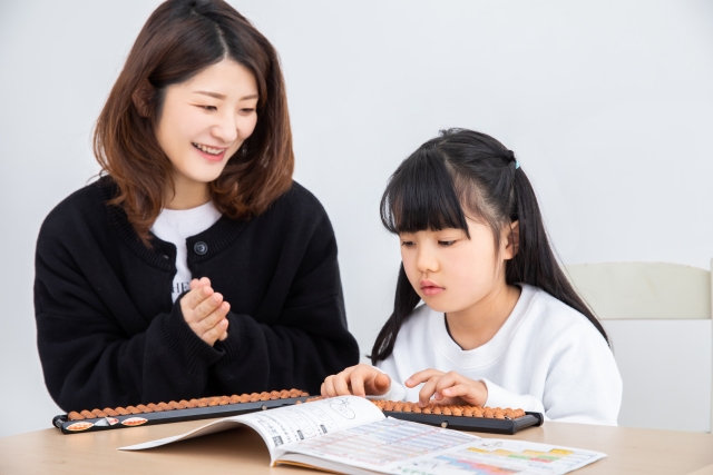 子供がそろばんの練習をして母親が褒めている
